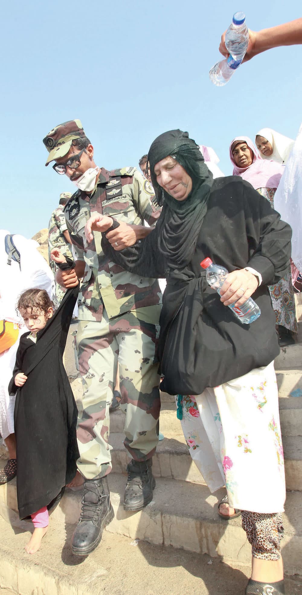 رجل أمن يقدم المساعدة لإحدى الحاجات وابنتها في مشعر عرفة أمس.
 تصوير: عدنان مهدلي - «الاقتصادية»