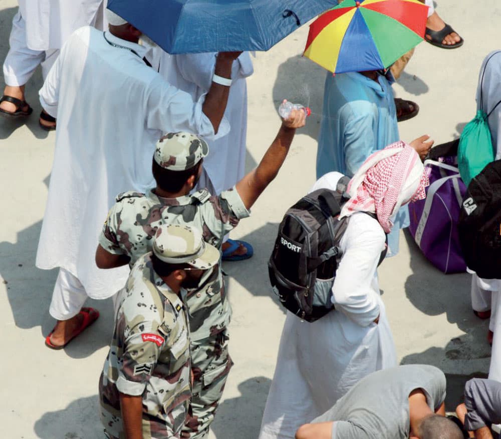 جندي يحاول تخفيف درجة الحرارة عن الحجيج برش المياه عليهم.