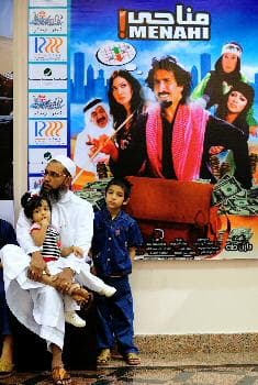 سعودي وأولاده ينتظرون بجوار الملصق الخاص بالفيلم السعودي (مناحي) خارج أحد المسارح في جدة حيث شهد حضوراً كثيفاً