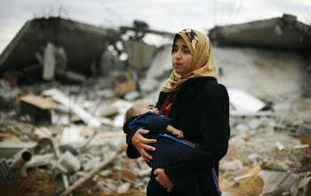 تهاني الفلسطينية تحمل طفلتها الصغيرة وهي ترى المنازل المدمرة في جنوبي قطاع غزة