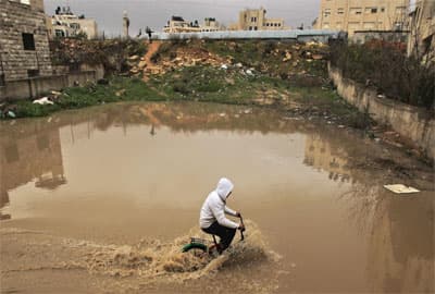 صبي فلسطيني يشق بدراجته طريق فاضت به مياة الأمطار في مدينة رام الله.