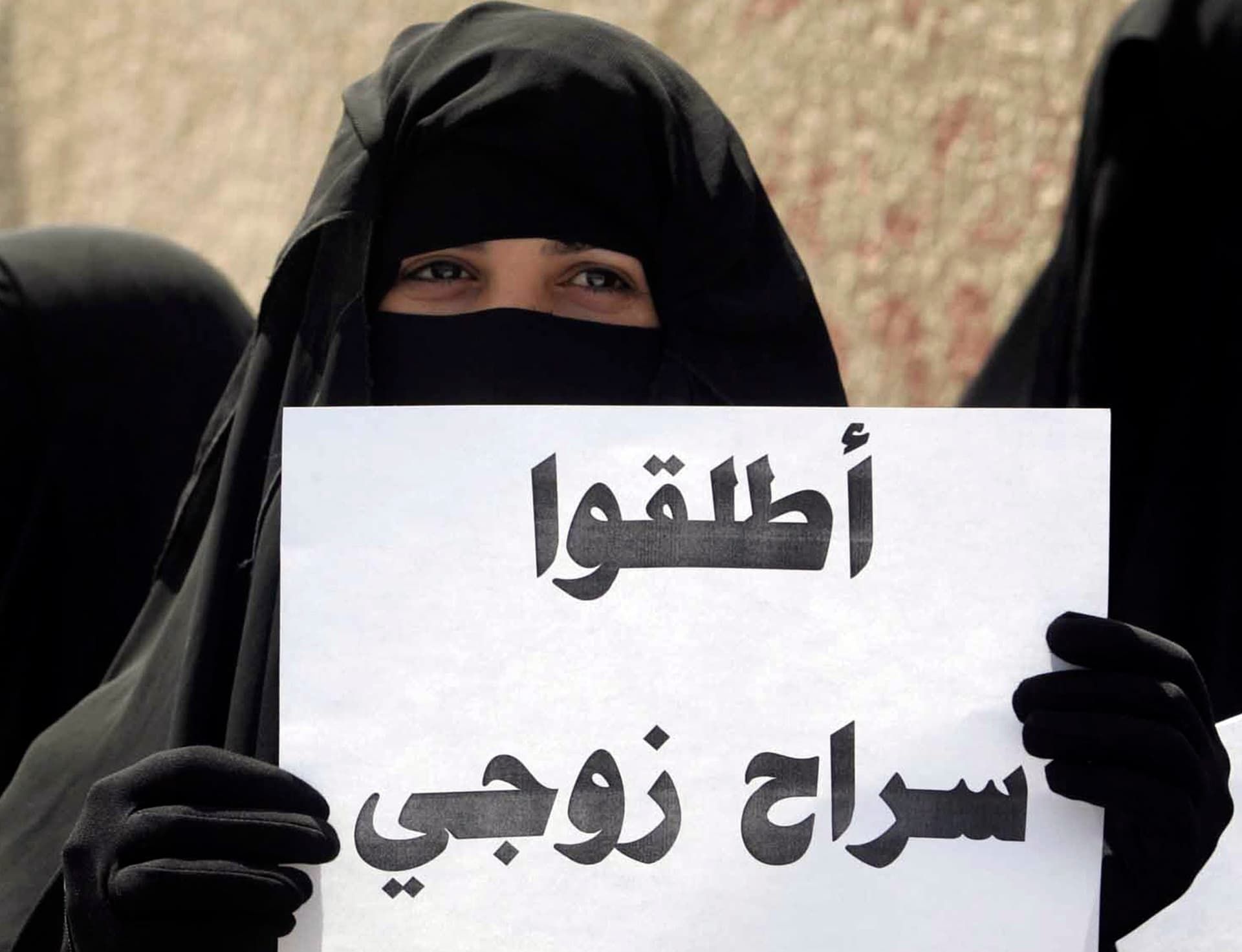امرأة تحمل لافتة كتب عليها "أطلقوا سراح زوجي" خلال مظاهرة احتجاج شارك فيها أكثر من 200 من النساء والأطفال للمطالبة بالإفراج عن ا