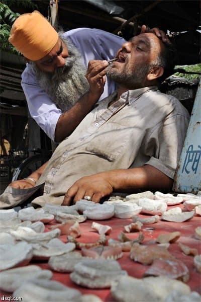 طبيب الأسنان الهندي سينغ يعالج مريض في عيادته (كشك) على جانب طريق رئيسي  في أمريتسار.
