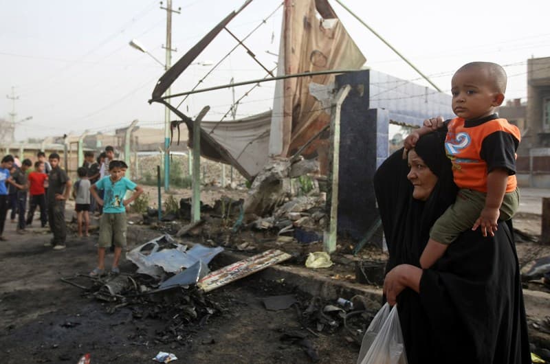 امرأة عراقية تحمل طفلها على كتفيها وتتفقد الأضرار أثر انفجار سيارة مفخخة في بغداد