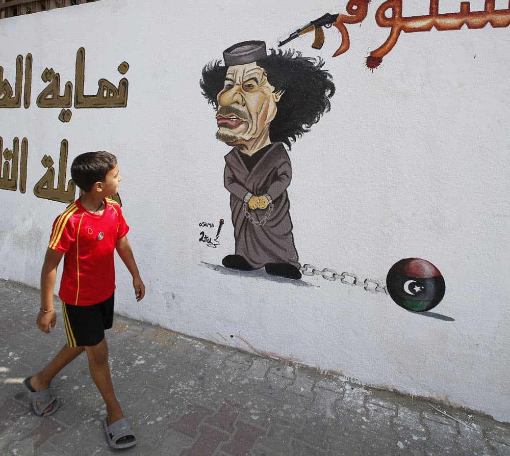صبي ليبي يمشي بجانب رسما كاريكاتوريا يسخر من معمر القذافي في العاصمة الليبية طرابلس