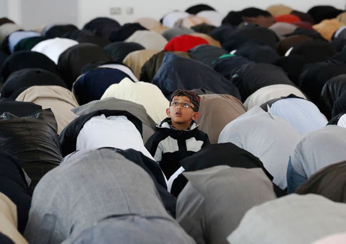 طفل مع والده يجلسان بقرب رفوف الأحذية للاستماع لخطبة في أحد مساجد لندن