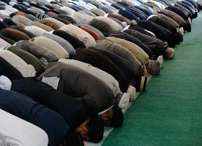 طفل مع والده يجلسان بقرب رفوف الأحذية للاستماع لخطبة في أحد مساجد لندن