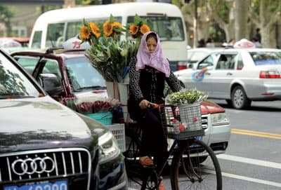 بائعة زهور تسير بدراجتها الهوائية بين السيارات في أحد شوارع منطقة شنغهاي الصينية