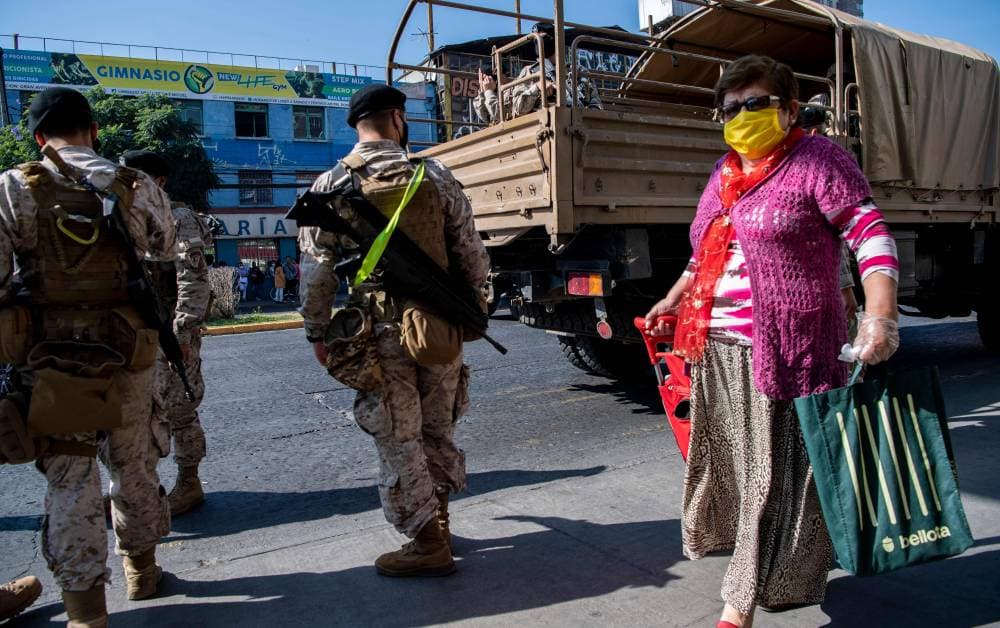 إمرأة تحمل أغراضها تمر من أمام دورية عسكرية وسط سانتياجو. "الفرنسية"