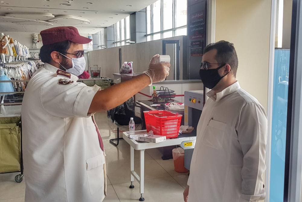 فرد أمن يقيس درجة حرارة متسوق في مدخل مركز تجاري. "واس"