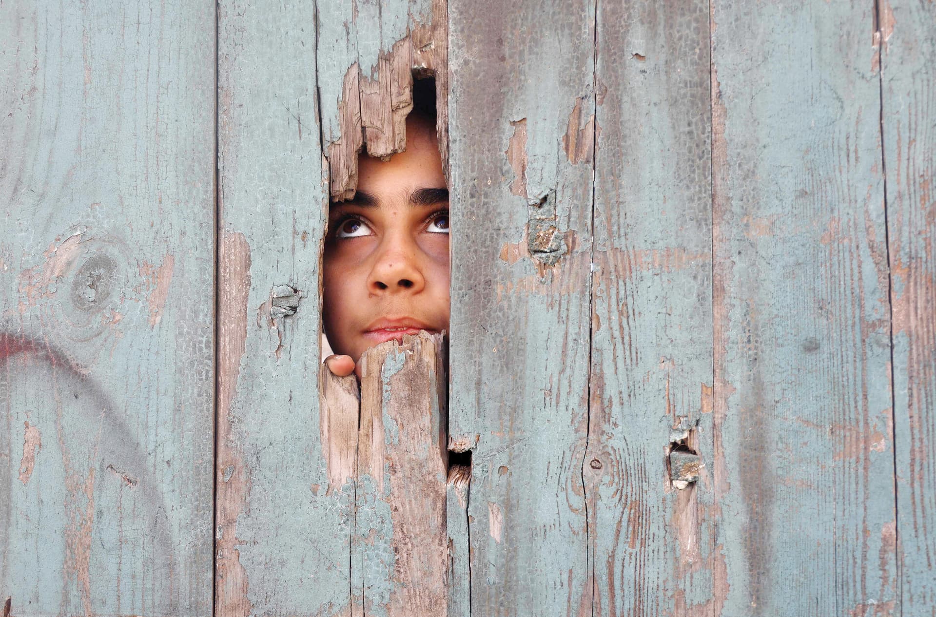طفلة تنظر عبر ثقب في باب منزلها شمال قطاع غزة 