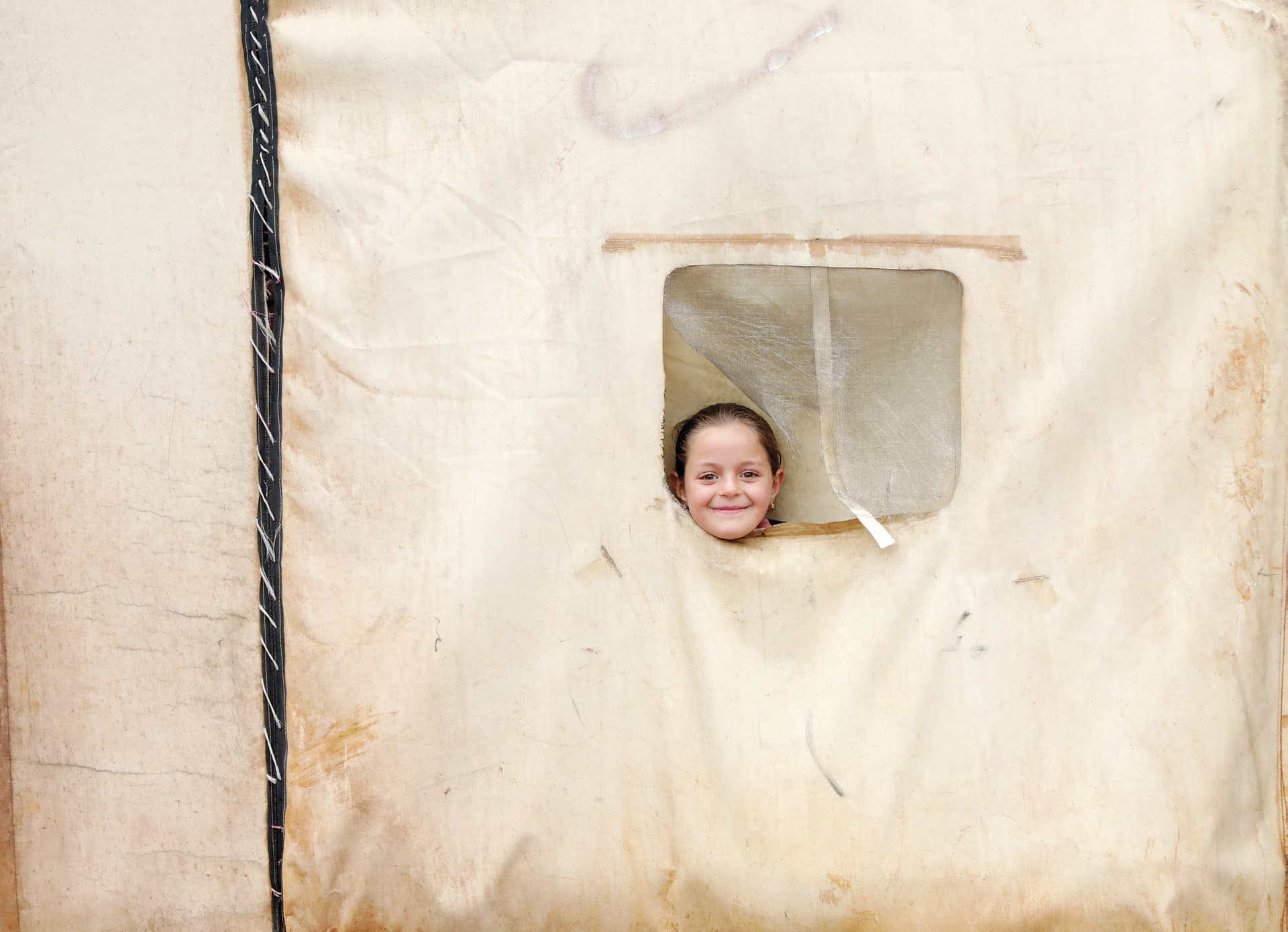 طفلة سورية تنظر من نافذة مخيم للاجئين شمال حلب