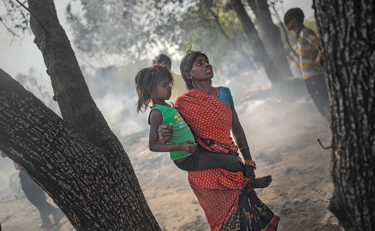 امرأة تحمل ابنتها بعيدا عن آثار حريق اندلع في إحدى ضواحي الهند الفقيرة
