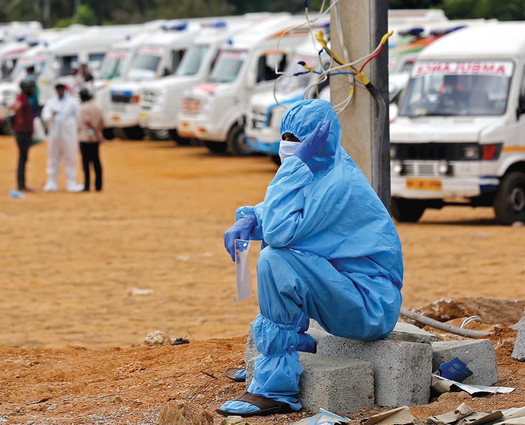 رجل يرتدي لباس الحماية الشخصية أثناء انتظاره لإحراق جثث أقاربه في موقع حرق جثث جماعية في مدينة بنجالور الهندية 