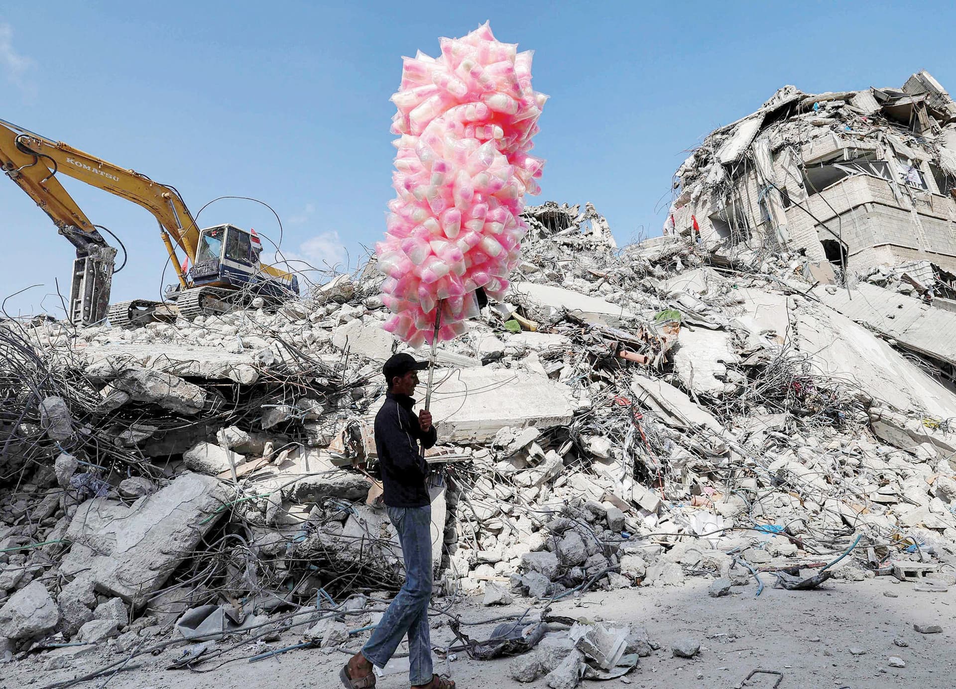 فلسطيني يسير بأكياس حلوى أمام أنقاض مبنى دمرته الغارات الإسرائيلية