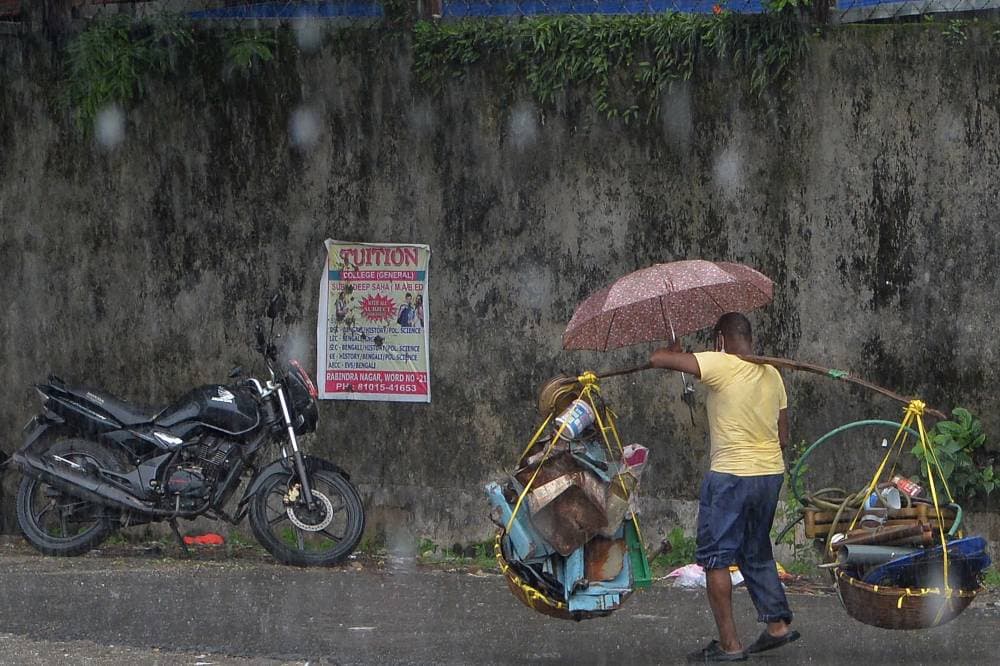 رجل يمشي حاملا أشياء قابلة لإعادة التدوير أثناء هطول الأمطار في سيليجوري الهندية."الفرنسية"