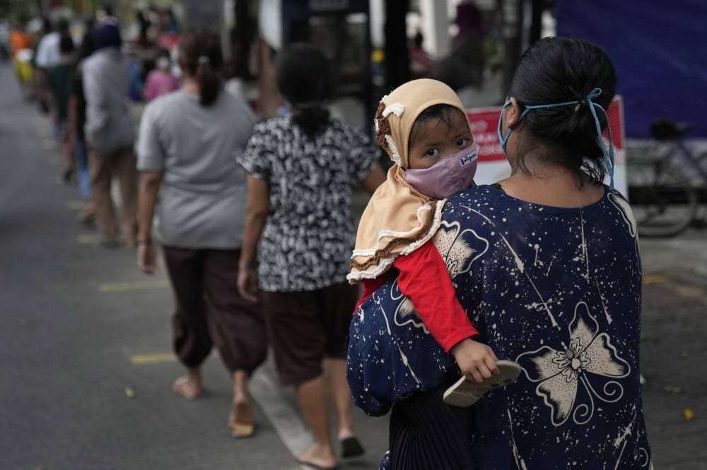 امرأة تحمل ابنتها وهي تصطف في طابور الإفطار المجاني في إندونيسيا.  "إ.ب.أ"