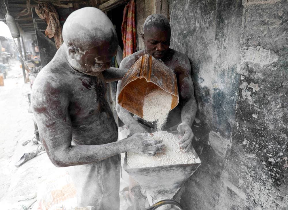 رجلان يقومان بطحن نبتة الكسافا المجففة وتحويلها إلى دقيق في متجرهما في سوق بوديجا في نيجيريا التي تشتهر بهذه النبتة. «رويترز»