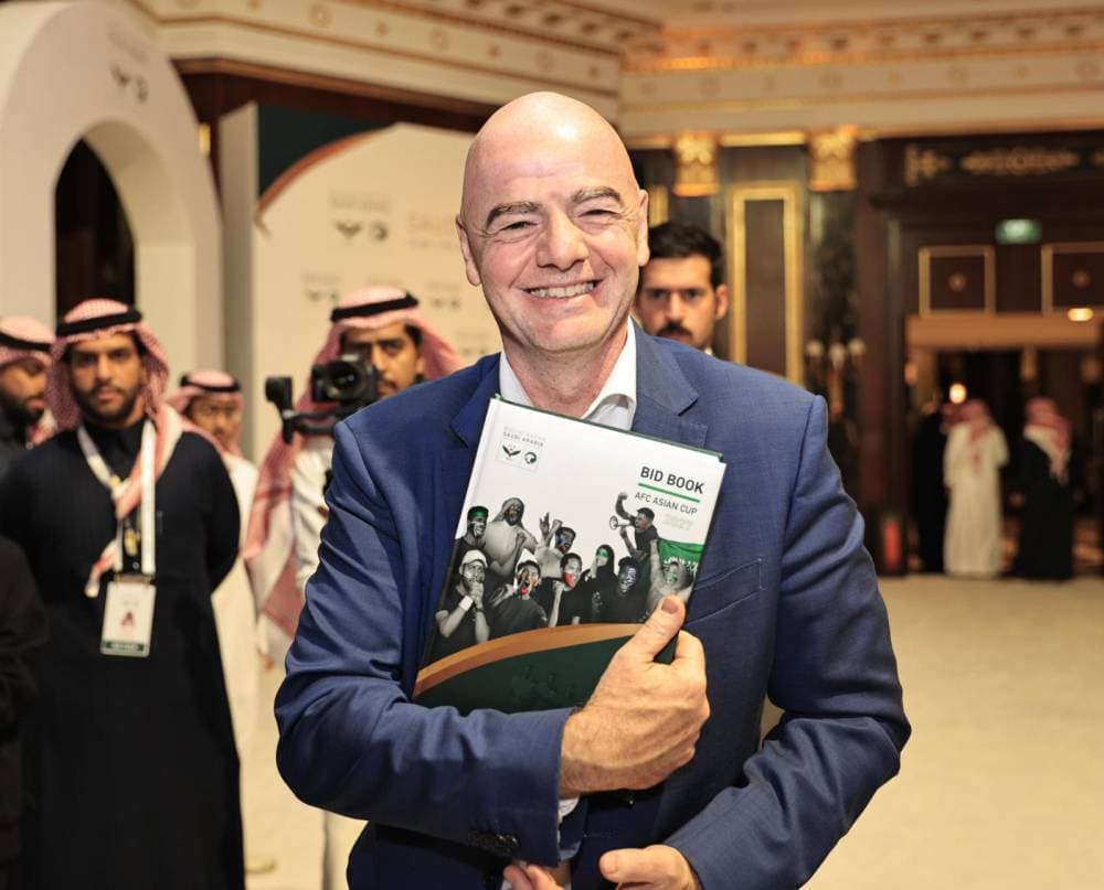 رئيس «فيفا» يحمل كتابا عن المشاركات السعودية في آسيا.