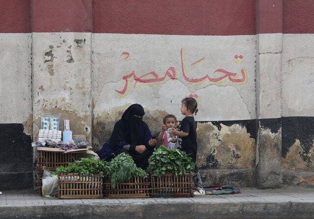 بائعة متجولة تجلس مع أطفالها أمام لوحة جدارية تصور العلم الوطني المصري في العاصة القاهرة. "رويترز"