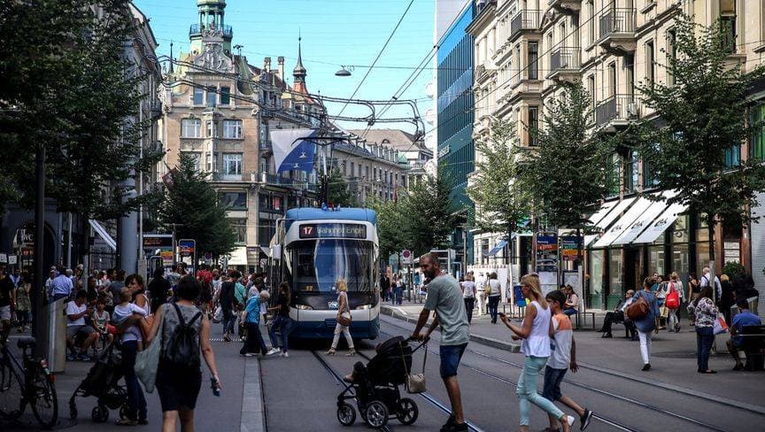 شارع حيوي يعج بالمارة ويمر به ترام، ويحيطه مبانٍ تاريخية وأجواء سياحية نابضة في زيورخ، سويسرا. "جيتي"