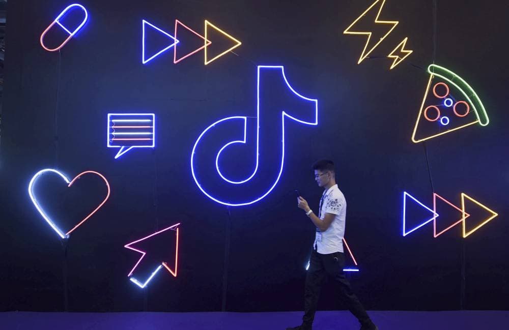 A man uses his smartphone as he walks past a display for Douyin, the Chinese version of video-sharing app TikTok, at an expo in Hangzhou in eastern China's Zhejiang Province, Oct. 18, 2019. President Donald Trump on Thursday, Aug. 6, 2020, ordered a sweeping but unspecified ban on dealings with the Chinese owners of consumer apps TikTok and WeChat, although it remains unclear if he has the legal authority to actually ban the apps from the U.S. (Chinatopix via AP)