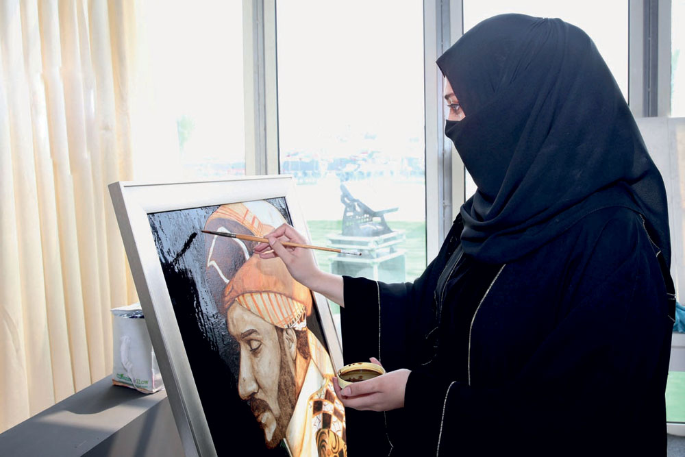 إحدى المشاركات تعرض إبداعاتها من لوحات رسم.
