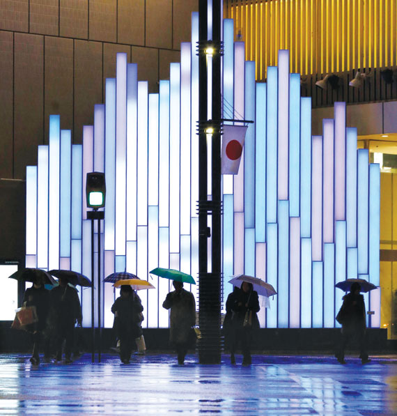 مشاة يرفعون مظلات بجوار شاشة مضيئة داخل منطقة تسوق في طوكيو