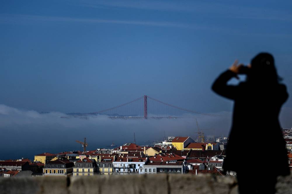 امرأة تلتقط صورة لجسر 25 أبريل المحاط بالغيوم وذلك من قلعة ساو جورج في لشبونة البرتغالية. "الفرنسية"