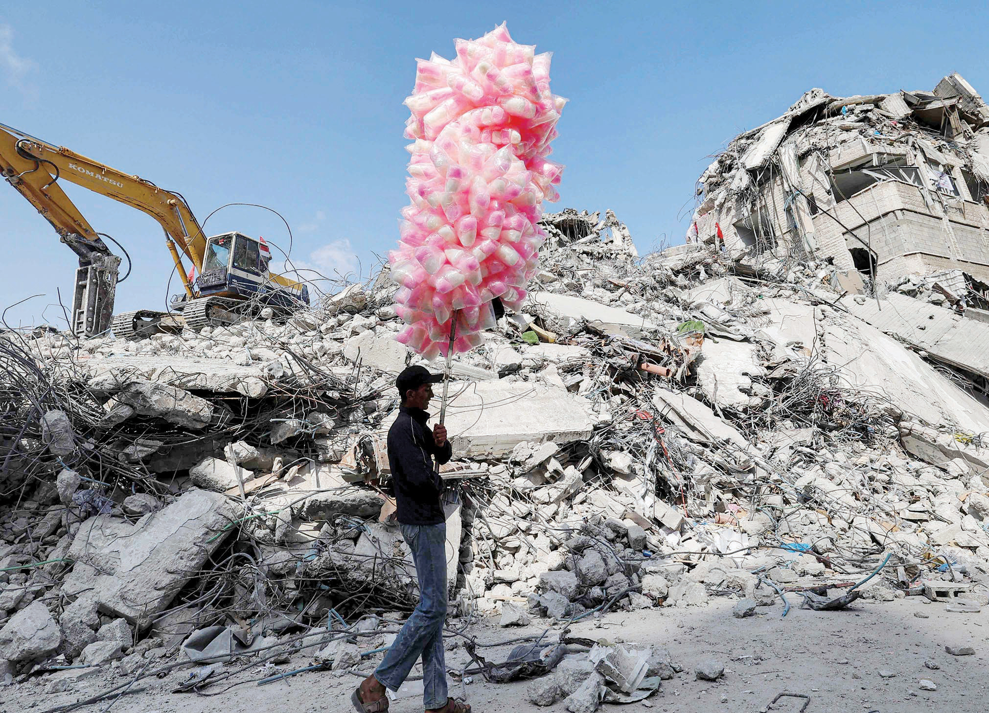فلسطيني يسير بأكياس حلوى أمام أنقاض مبنى دمرته الغارات الإسرائيلية