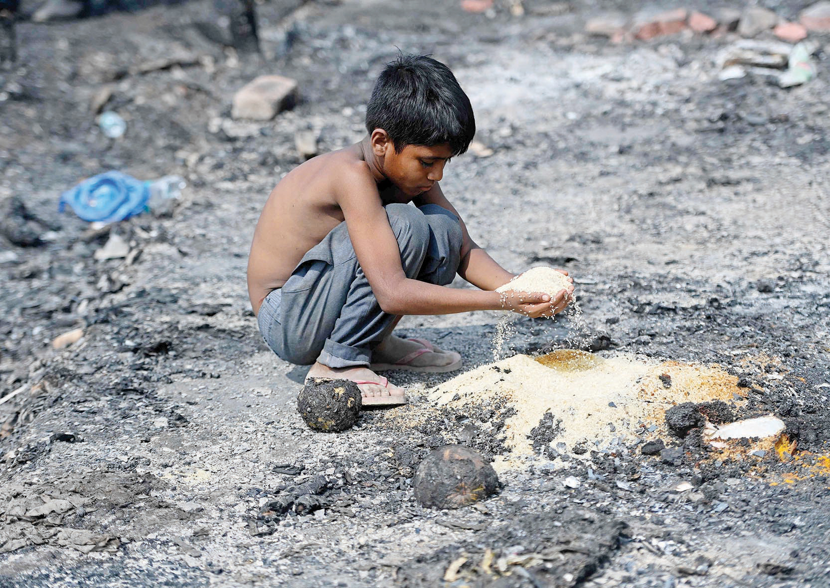 طفل من الروهينجا يلتقط حبوبا غذائية وسط بقايا مخيمهم المتفحم إثر حريق اندلع في نيودلهي
