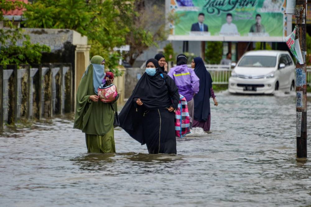 نساء يسرن عبر مياه فيضانات بعد هطول أمطار غزيرة على منطقة أجون في ضواحي مدينة باندا آتشيه الإندونيسية."الفرنسية"