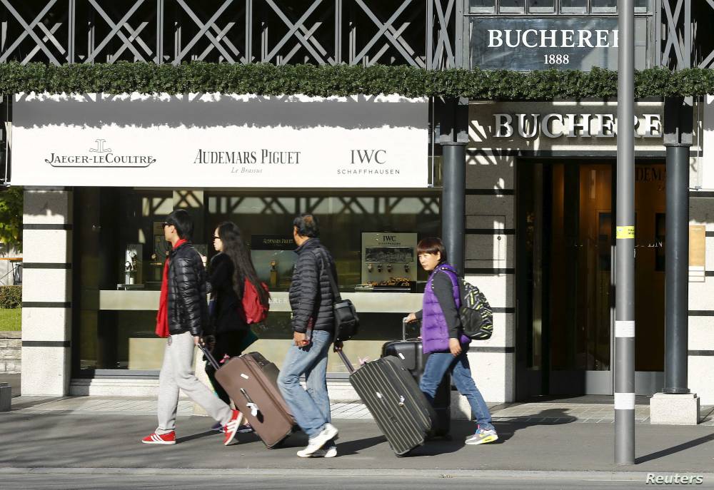 سياح آسيويون يمرون من أمام متجر للساعات في منطقة جبال الألب في سويسرا. تصوير: روبن سبرتش "رويترز"