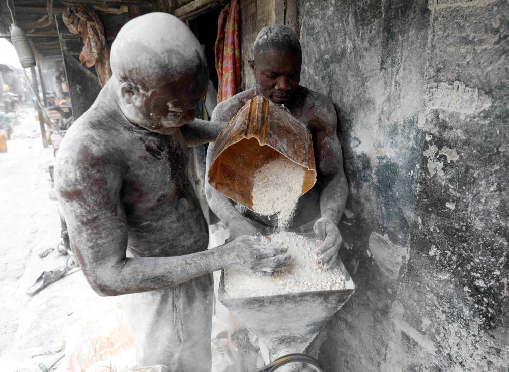 رجلان يقومان بطحن نبتة الكسافا المجففة وتحويلها إلى دقيق في متجرهما في سوق بوديجا في نيجيريا التي تشتهر بهذه النبتة. «رويترز»