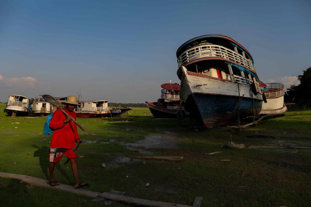  رجل يسير بجوار قوارب تقطعت بها السبل في بحيرة إليكسو بسبب الجفاف الشديد في ولاية أمازوناس، فنزويلا. "الفرنسية"