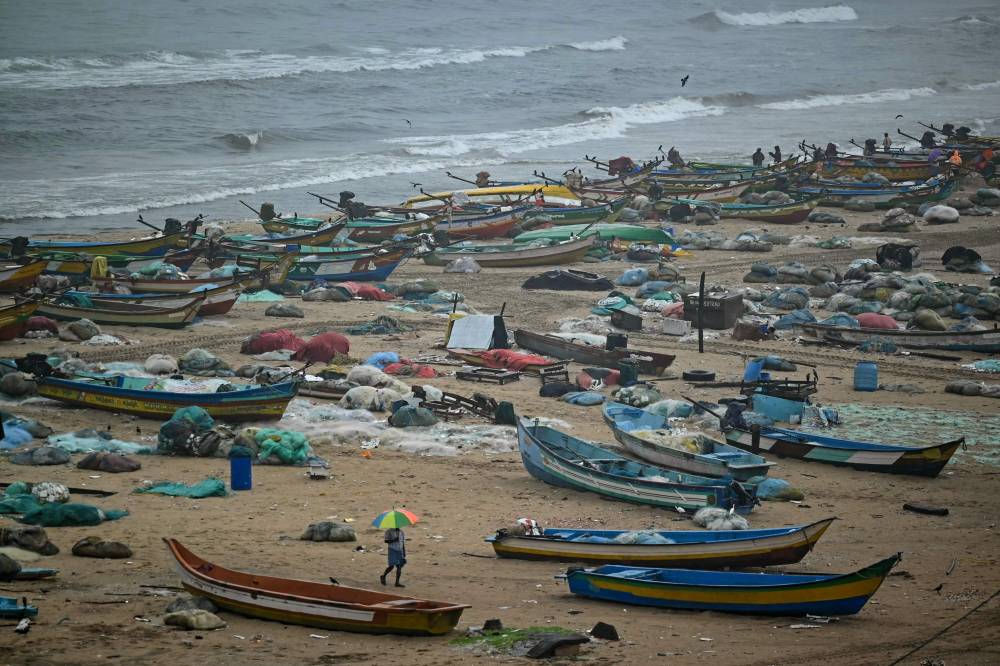  رجل يحمل مظلة يسير بجوار قوارب راسية على شاطئ مارينا، حيث يتوقف الصيد حتى انتهاء هطول الأمطار في تشيناي، الهند. "الفرنسية" 
