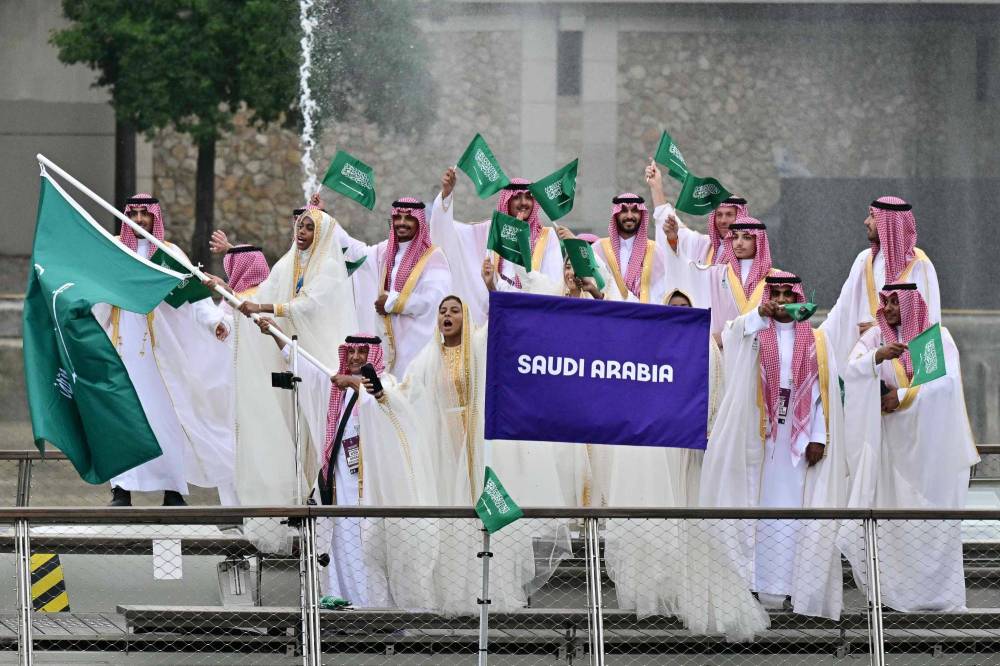 يلوح رياضيون من وفد السعودية بالأعلام أثناء إبحارهم على متن قارب على طول نهر السين. الفرنسية