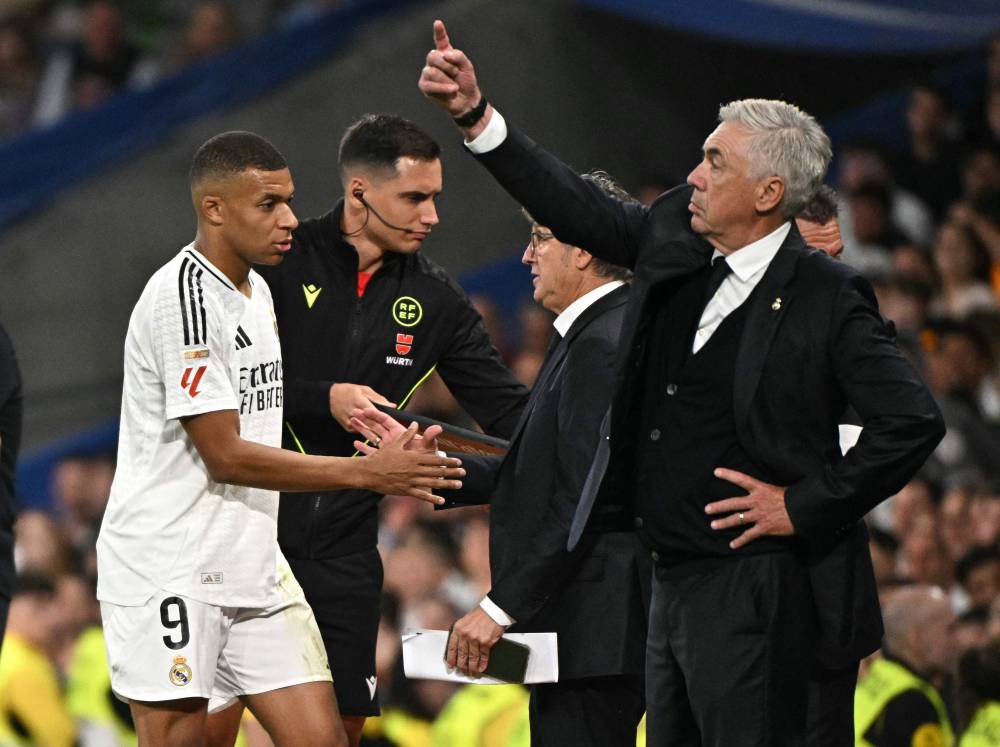 Real Madrid's French forward #09 Kylian Mbappe (L) walks next to Real Madrid's Italian coach Carlo Ancelotti as he leaves the pitch during the Spanish league football match between Real Madrid CF and Deportivo Alaves at the Santiago Bernabeu stadium in Madrid on September 24, 2024. Real Madrid striker Kylian Mbappe has sustained a thigh injury to the biceps femoris in his left leg, ahead of this weekend's La Liga derby clash against Atletico, his club announced. The French superstar was taken off during the 3-2 win over Alaves on September 24 and appeared to be suffering some discomfort. (Photo by JAVIER SORIANO / AFP)