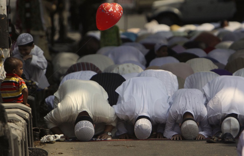 طفل يحمل بالونا وينظر إلى مصلين يؤدون صلاة عيد الفطر في الهند اليوم حيث أعلنت بعض الدول الإسلامية ومنها الهند أن يوم الإثنين هو 