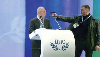 صورة تلفزيونية تظاهر رجلا يوجه سلاحه على أحمد دوجان رئيس حزب العدالة والحرية في بلغاريا أثناء إلقاء كلمته في حفل الكونجرس البلغا