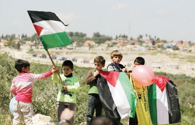 أطفال فلسطينيون يحملون أعلام  بلدهم أمس ضمن الاحتفالات بيوم الأرض بالقرب من إحدى المستوطنات اليهودية