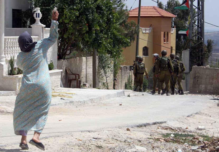 امرأة تلقي الحجر تجاه الجنود الاسرائيليين خلال اشتباكات عقب احتجاج ضد مصادرة الأراضي الفلسطينية من قبل إسرائيل