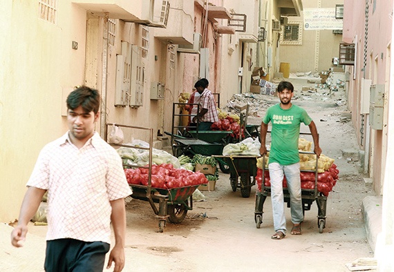 عمالة تقوم بحمل كميات من الخضار من أحد شوارع حي البطحاء وسط الرياض تمهيدا لبيعها على الأرصفة بطريقة عشوائية