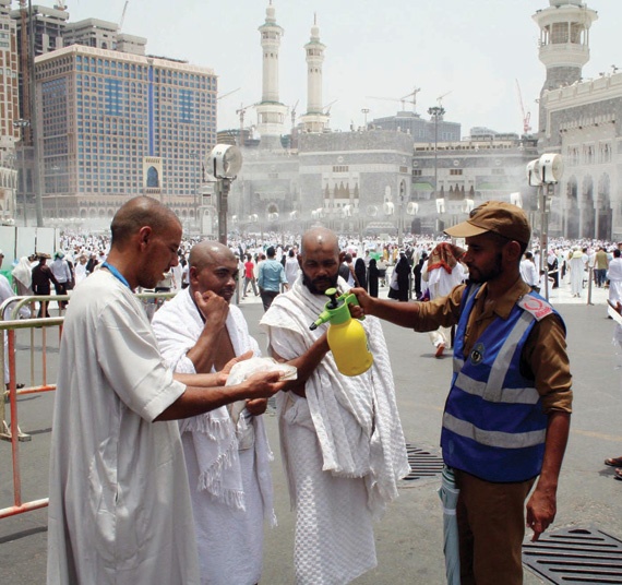 أحد أفراد أمن الحرم يساعد معتمرين على ترطيب وجوههم من الحر