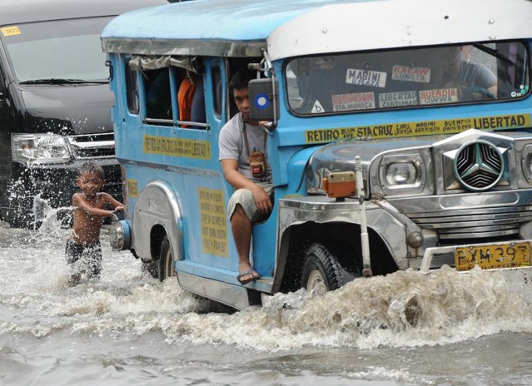 صبي فيليبيني يلعب خلف حافلة نقل في شارع اكتسحته الفضيانات بعد امطار غزيرة في مانيلا