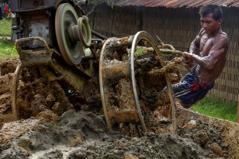 عامل يخلط مواد لصنع الطوب في أحد المصانع في ضواحي مدينة كاجو الإندونيسية