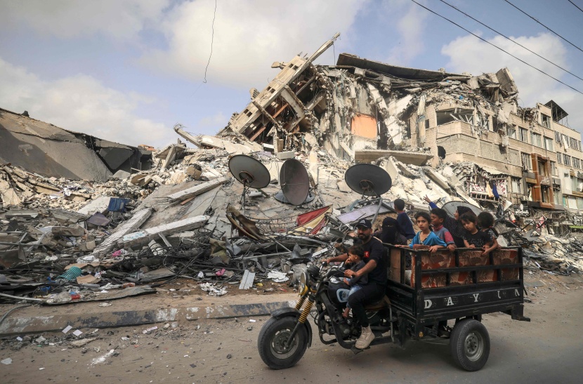 فلسطيني ينقل الأطفال بدراجة ثلاثية أمام مبنى دمرته غارة جوية إسرائيلية في غزة