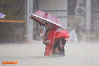 امرأة مع طفلين تمشي في شارع غمرته المياه أثناء هطول الأمطار في مدينة سيلهيت البنجلادشية